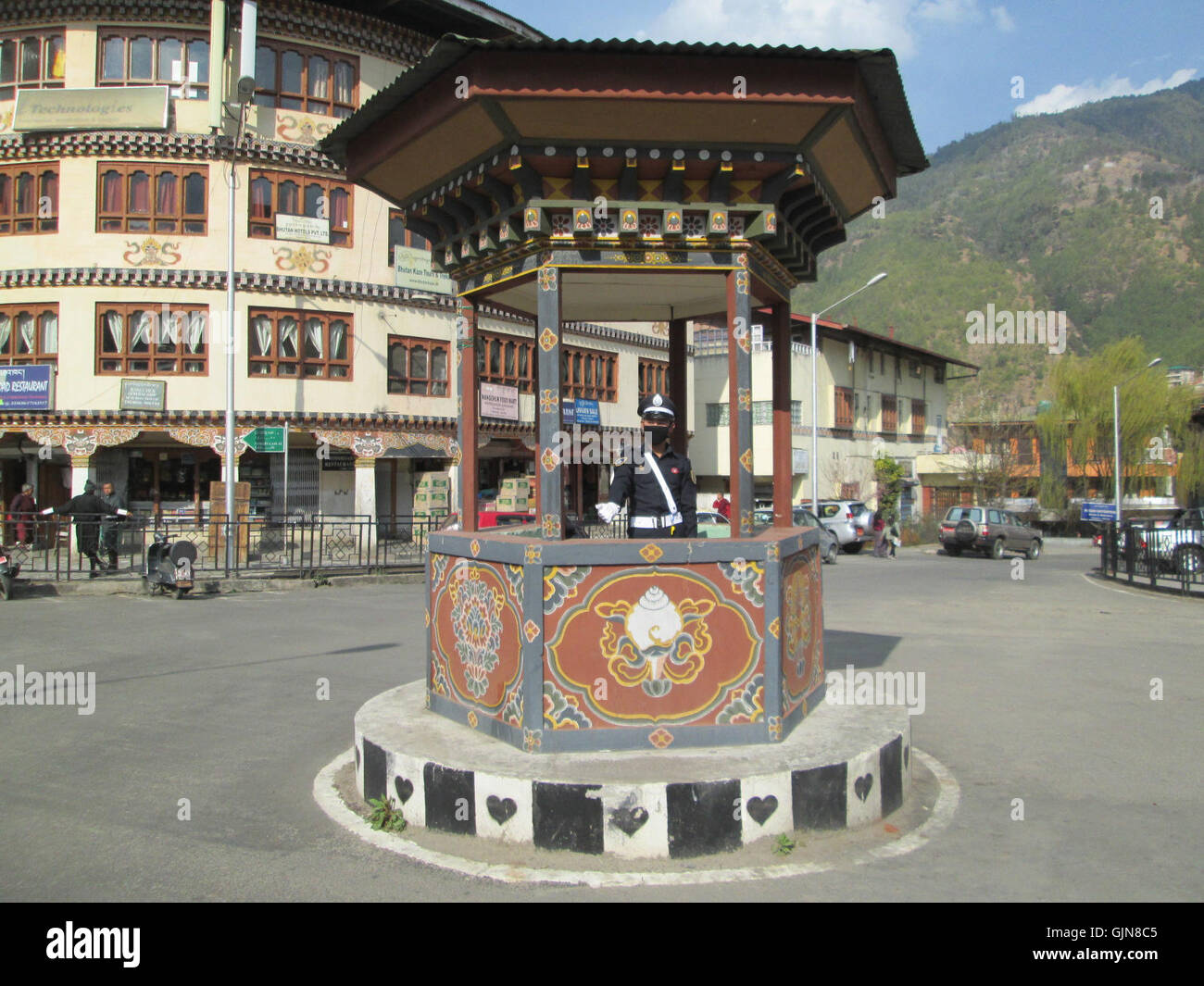 Ein Foto eines Verkehrspolizisten, der den Verkehr auf der Norzin Lam Road in Thimphu, Bhutan, verwaltet. Diese Szene reflektiert das tägliche Leben und die Rolle der Strafverfolgungsbehörden im städtischen Verkehrsmanagement in der Hauptstadt Bhutans. Stockfoto