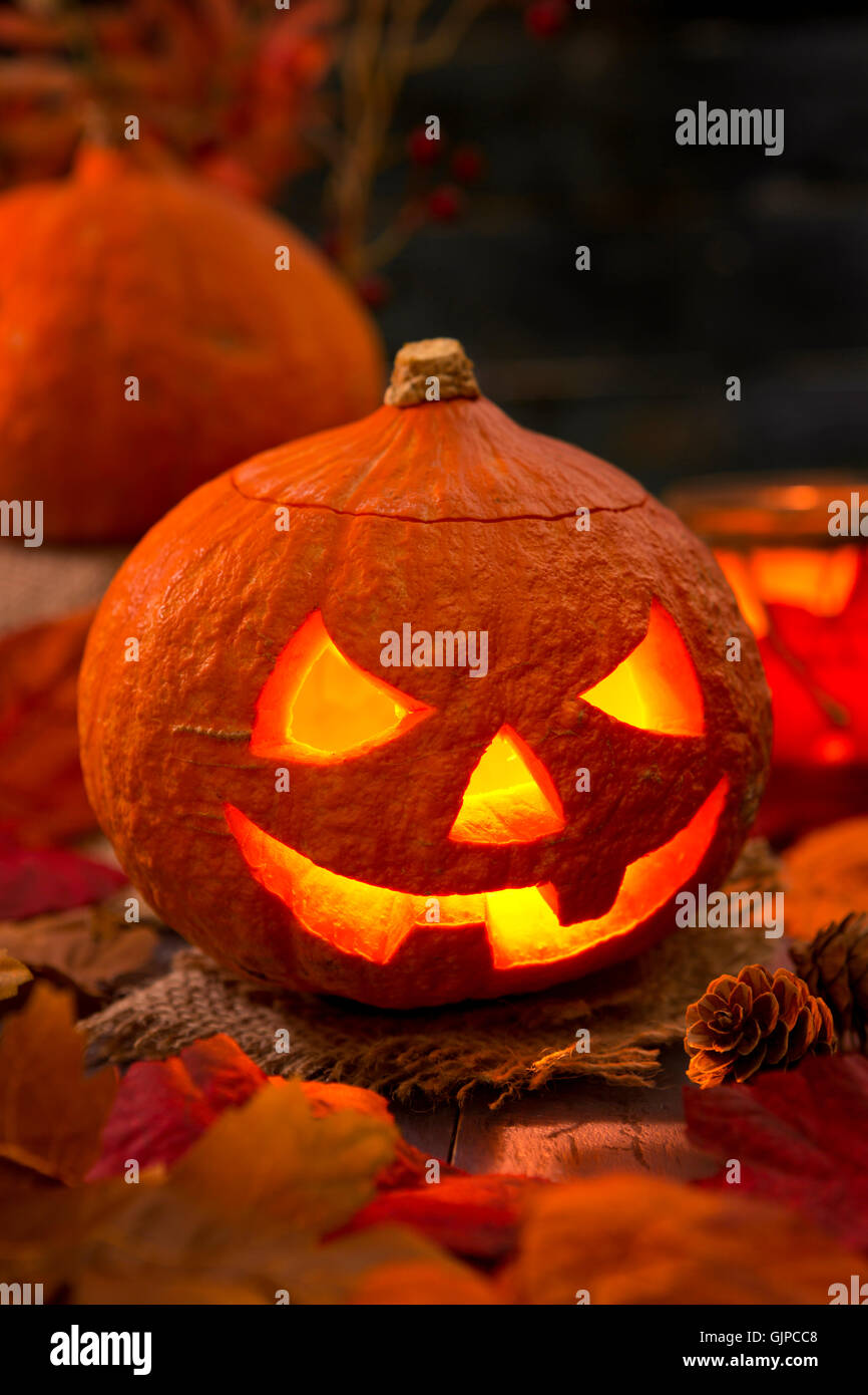 Brennen von Jack O'Lantern auf einem rustikalen Tisch mit herbstlichen Dekorationen, beleuchtet dunkel. Stockfoto