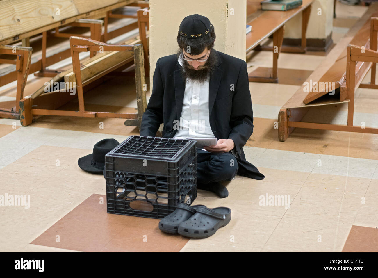 Ein religiösen jüdischer Mann sitzt auf dem Boden auf Tisha B'Av, beten ein Tag der Trauer auf dem hebräischen Kalender. Brooklyn, New York. Stockfoto