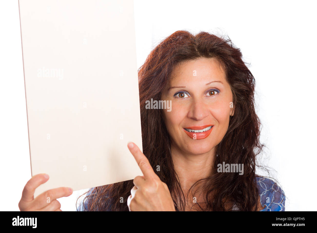 Happy Reife Frau mit arabischen und nahöstlichen somatische Merkmale und gefärbt mit Henna Haare lächelt ihr Finger auf leeren weißen Schild, den sie im Hochformat hält Stockfoto