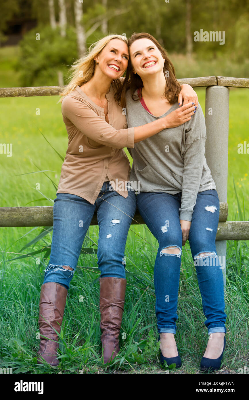 zwei Frauen umarmten einander und sitzen auf dem Zaun im freien Stockfoto