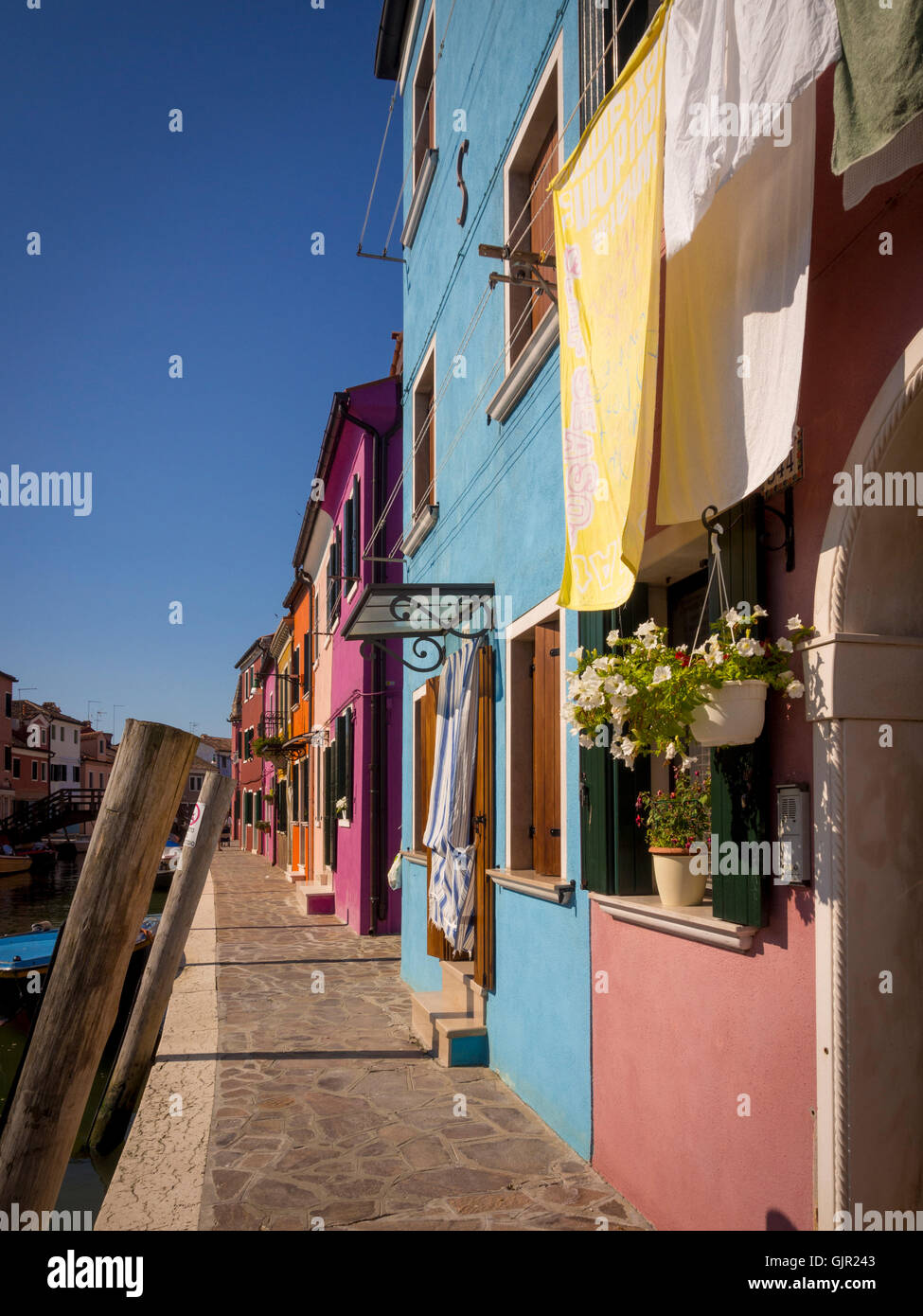 Hell gestrichene Häuser auf der Terrasse am Canalside mit Waschküche, die draußen an Wäscheleinen auf der Insel Burano hängt. Venedig, Italien. Stockfoto