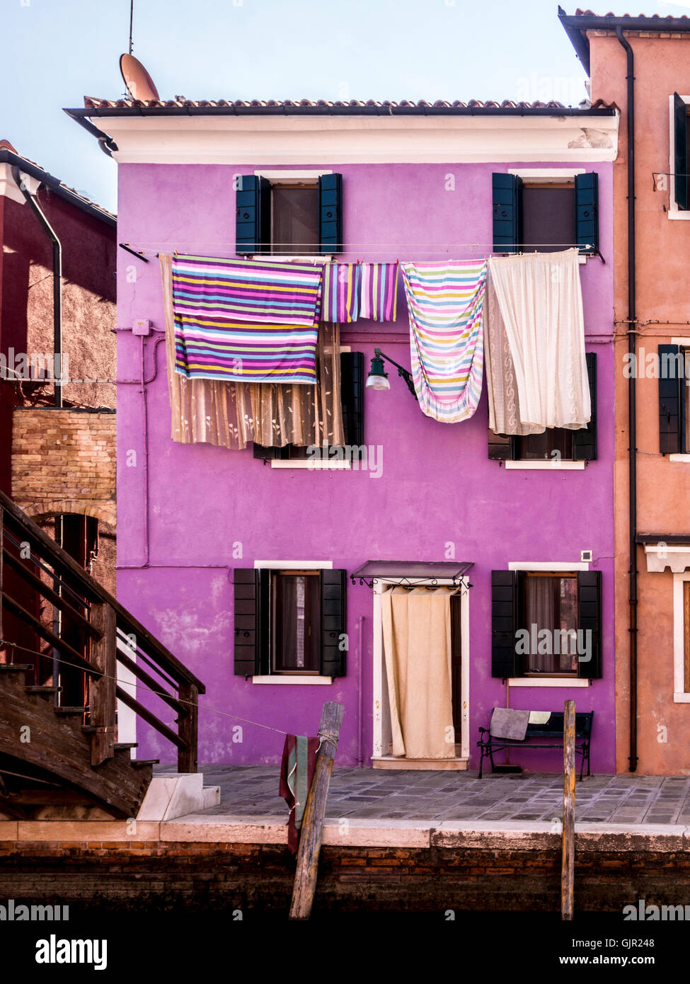 Violett gestrichenes Haus mit bunt gestreiften Wäschestüßen, die draußen an Wäscheleinen hängen. Insel Burano. Venedig, Italien Stockfoto