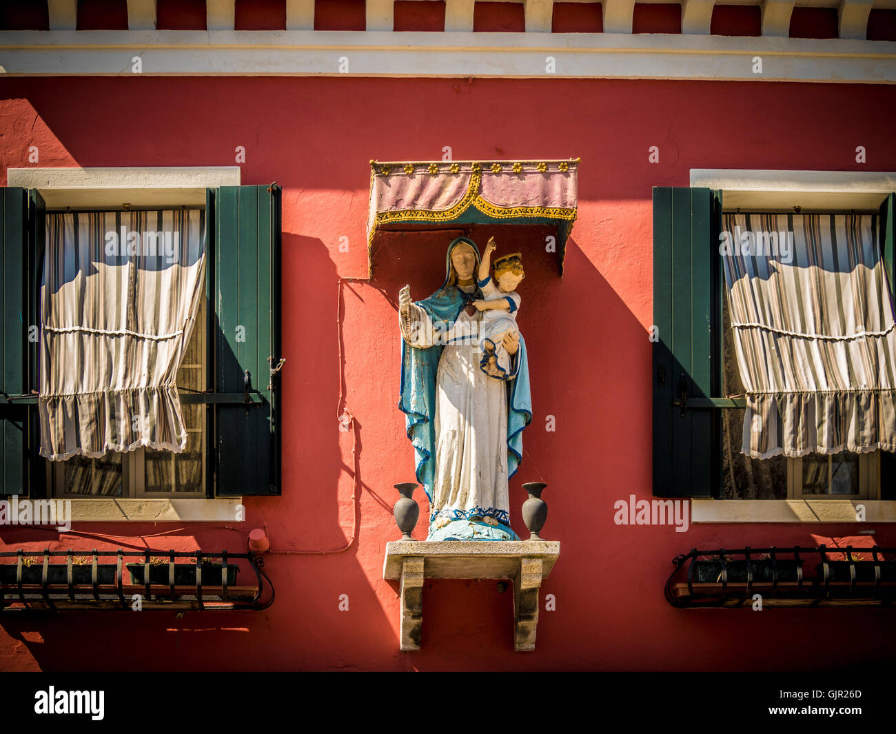 Madonna mit Kind Statue auf einer Terrakotta-farbigen Außenwand eines traditionellen Hauses auf der Insel Burano. Italien. Stockfoto