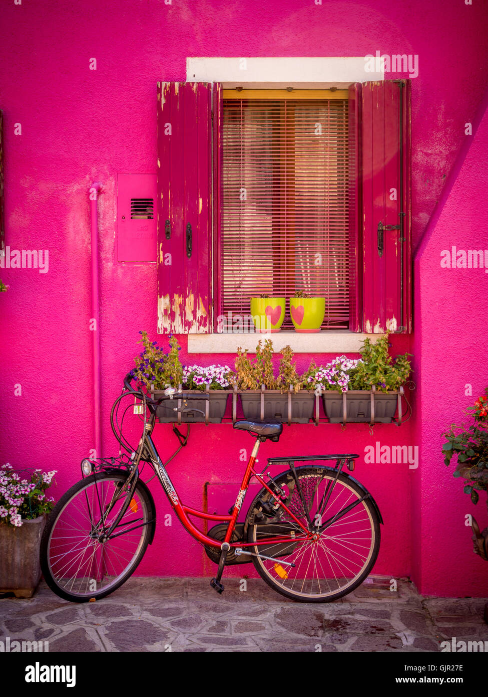 Helles rosafarbenes Haus mit einem Fahrrad, das draußen auf der Insel Burano geparkt ist. Venedig, Italien. Stockfoto