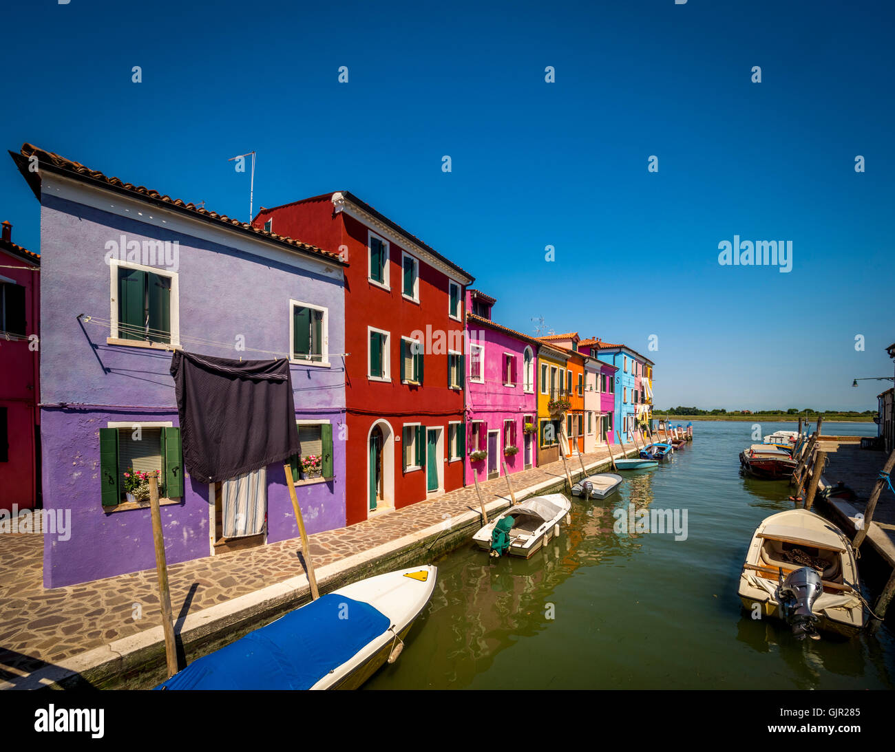 Reihe von traditionellen bunt bemalten Häusern an der Kanalseite mit Wäscheleinen, die draußen an Wäscheleinen hängen, auf der Insel Burano. Venedig Stockfoto