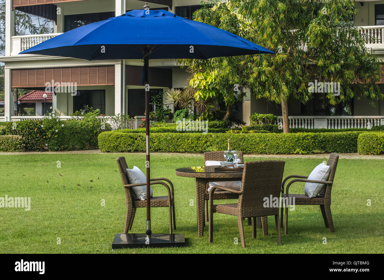 Rattan-Möbel, Tisch, Stühlen, Sonnenschirm und Outdoor-Kissen set im Garten Stockfoto