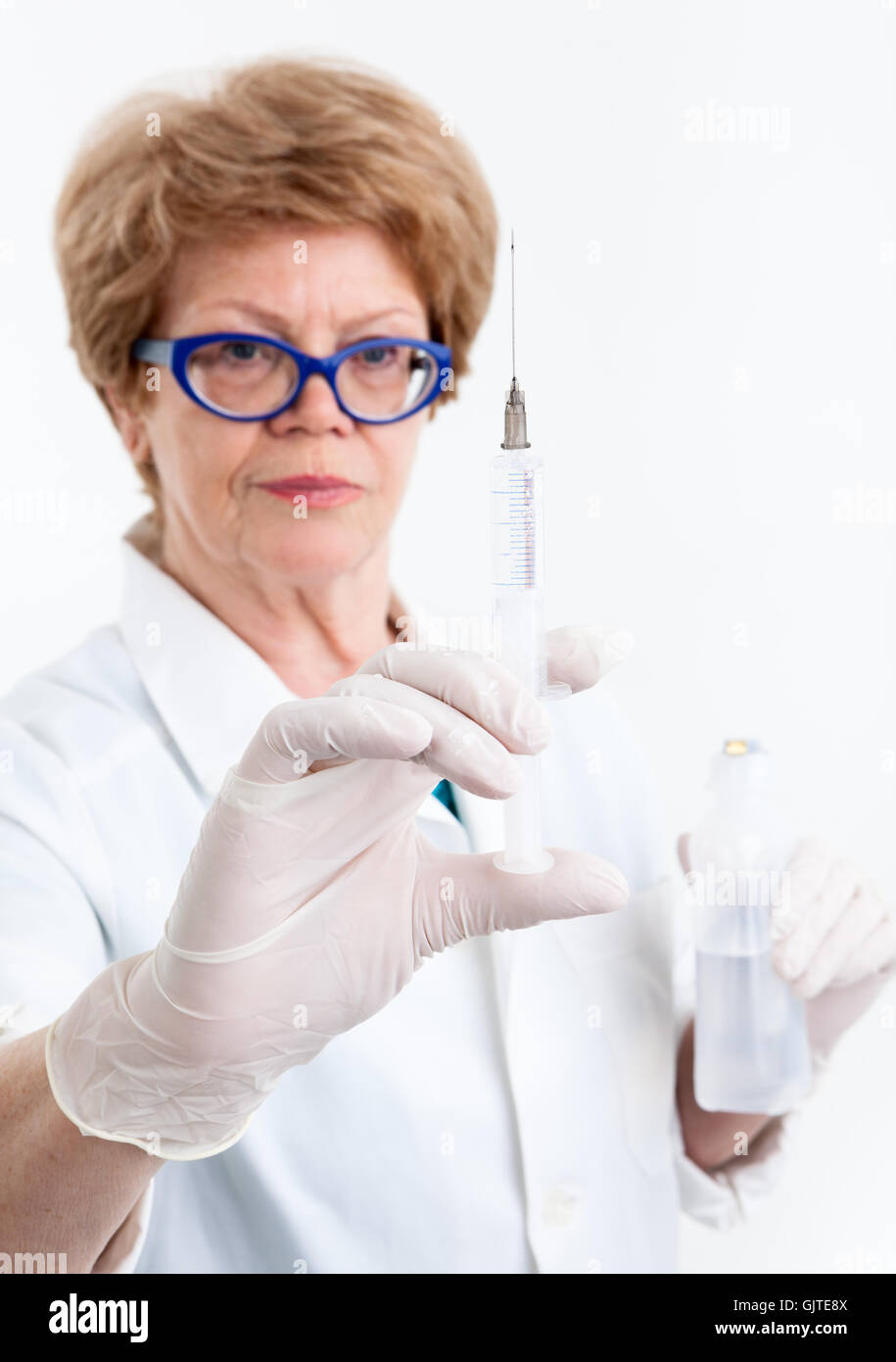 Ältere Frau Krankenschwester schaut Spritze zur Impfung in ihrer Hand, Fokus auf die Nadel, weißer Hintergrund Stockfoto