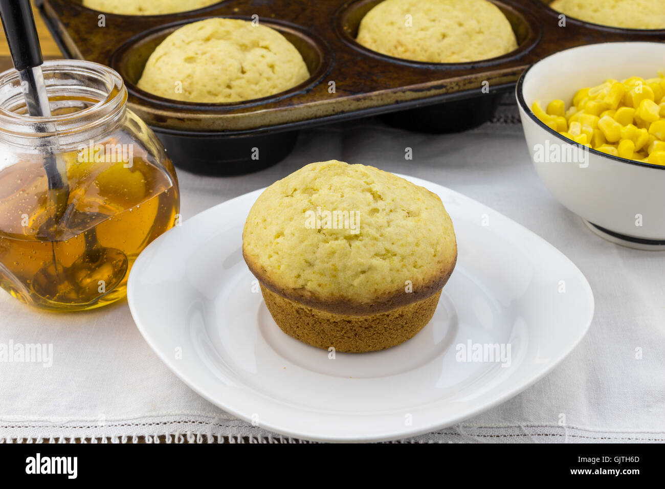 Foto von Mais Muffin in Platte mit Muffins in Pfanne, Sirup und Mais in einer Schüssel auf dem weißen Tuch Stockfoto