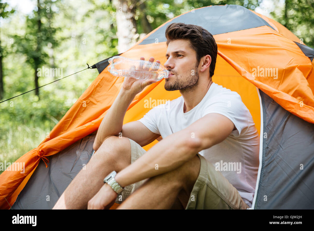 Hübscher junger Mann Touristen sitzen in touristische Zelt und Trinkwasser im Wald Stockfoto