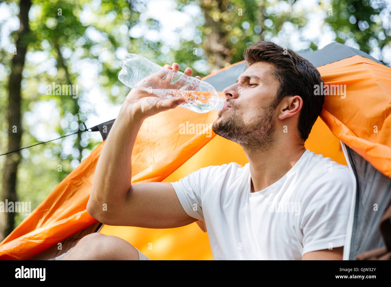 Nahaufnahme der attraktive junge Mann Touristen sitzen und Trinkwasser in touristische Zelt im Wald Stockfoto