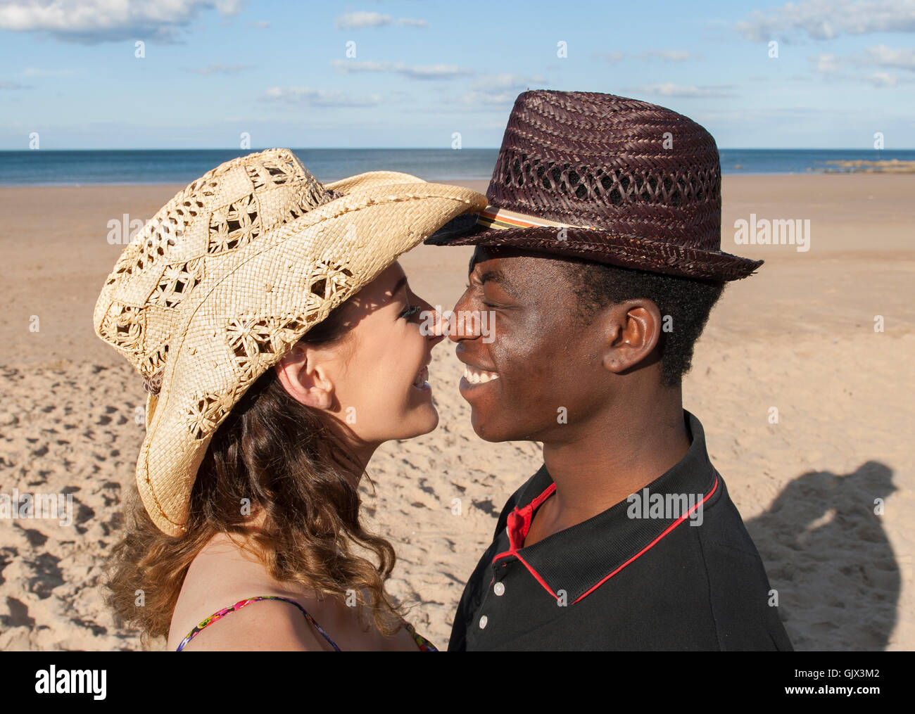 Attraktives Paar multikulturellen Mischlinge Kopf geschossen am Strand sahen einander lachend romantische Gefühle Liebe Hüte Stockfoto