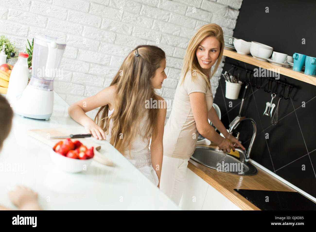 Mutter und Tochter vorbereiten und blending Smoothie aus frischen Früchten in der modernen Küche Stockfoto