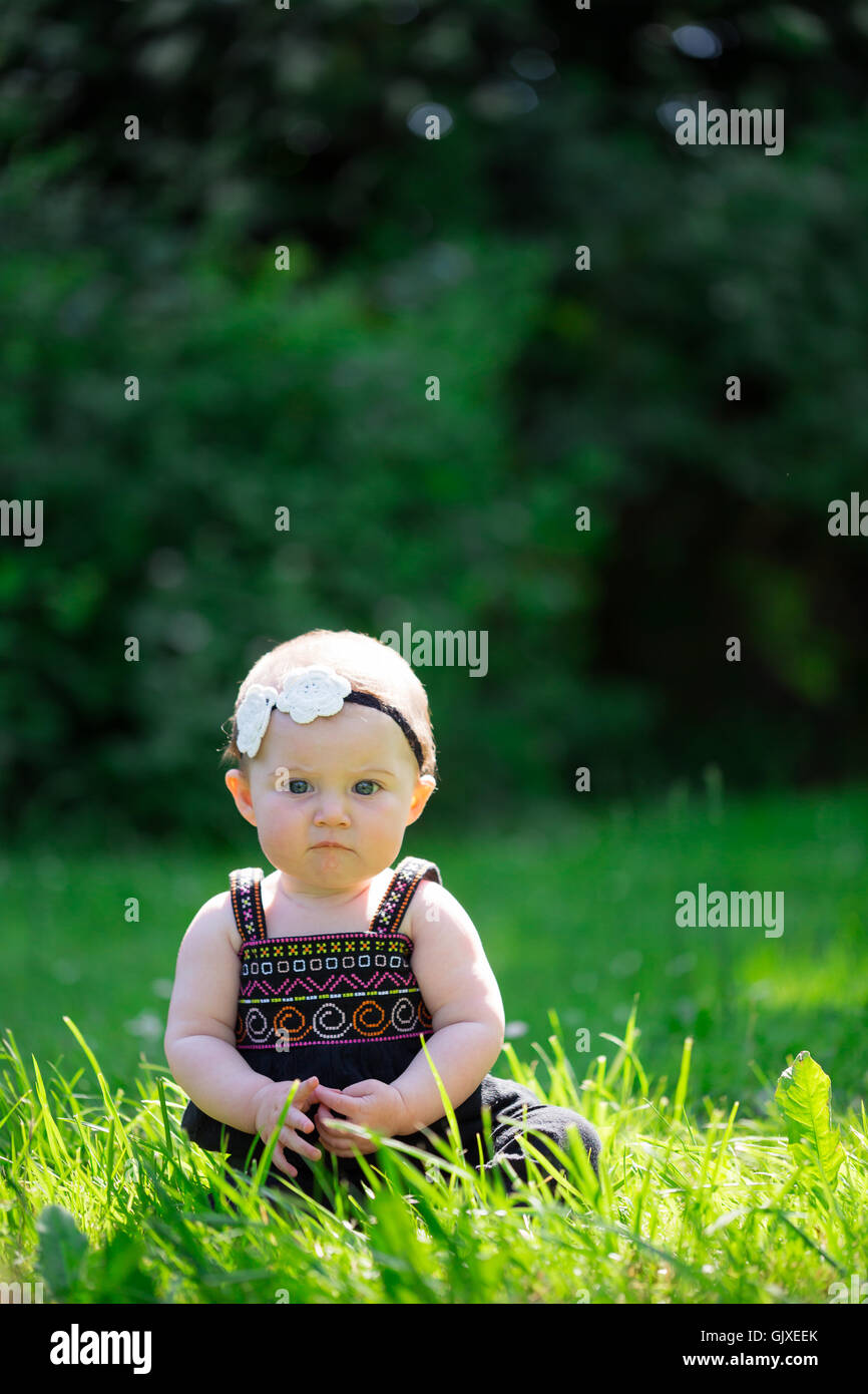 Babymädchen an etwa 6 Monate alt im Freien in einer natürlichen Umgebung mit vorhandenem Licht für ein Lifestyle-Porträt. Stockfoto