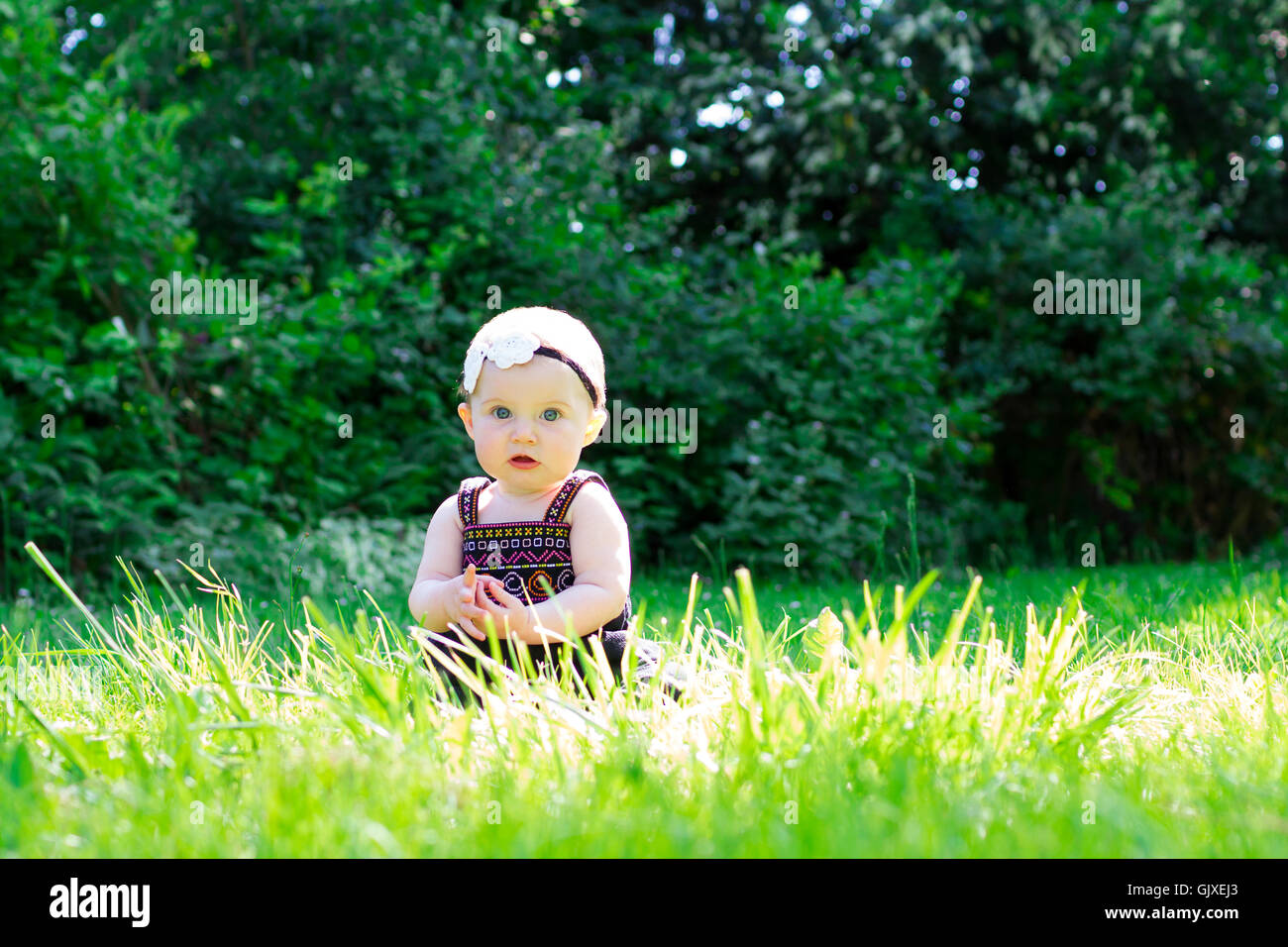 Babymädchen an etwa 6 Monate alt im Freien in einer natürlichen Umgebung mit vorhandenem Licht für ein Lifestyle-Porträt. Stockfoto