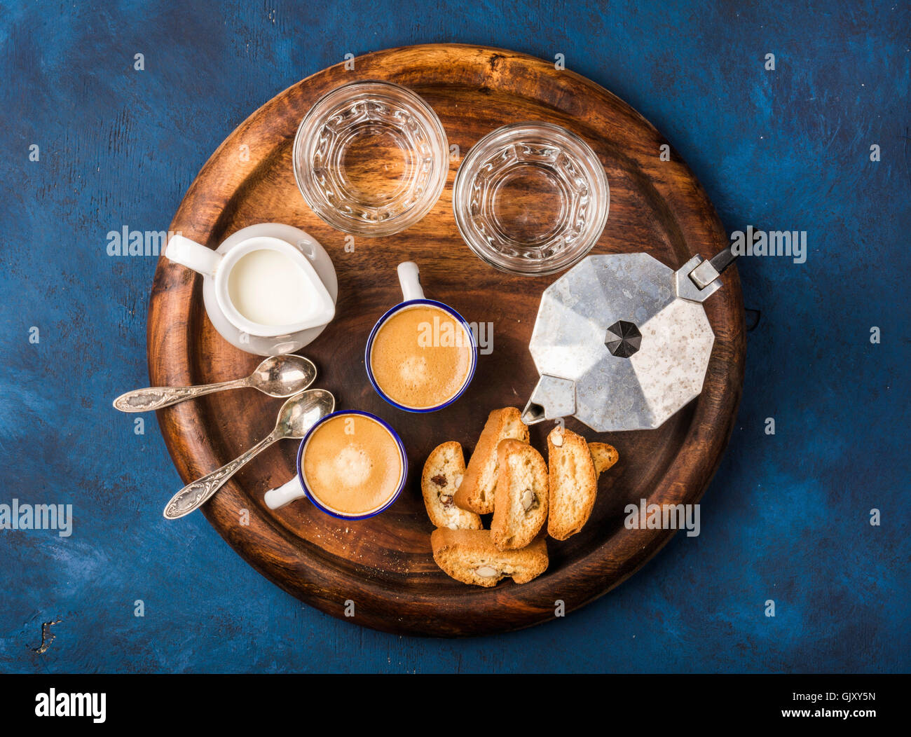Kaffee Espresso Tassen mit italienischen Cantucci, Kekse und Milch in der Kanne auf hölzernen dienen Runde Board über dunkel blau lackierten plyw Stockfoto