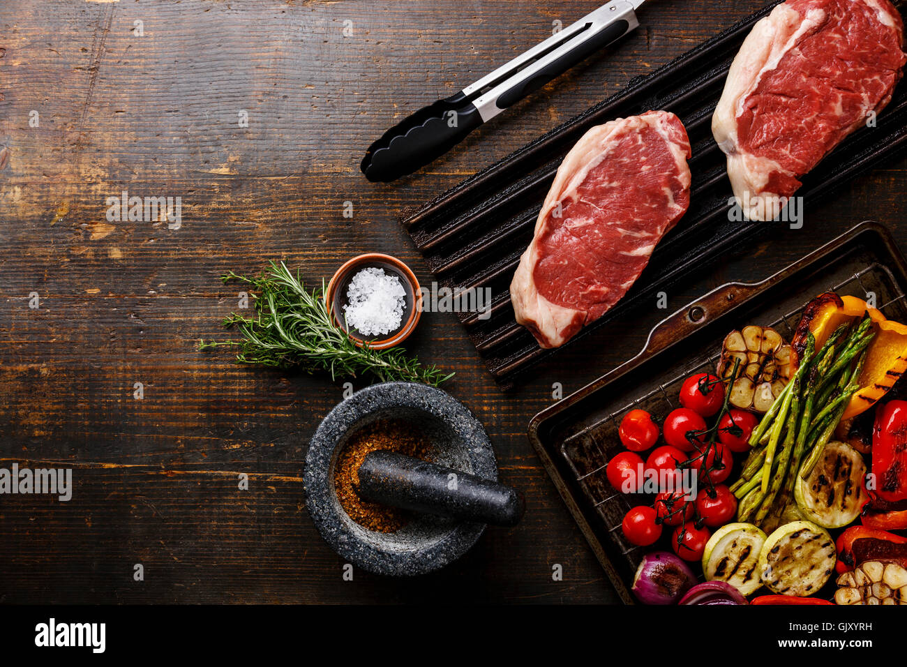 Rohes Frischfleisch Striploin Steak auf schwarzem Gusseisen Grill und gegrilltes Gemüse auf hölzernen Hintergrund Stockfoto