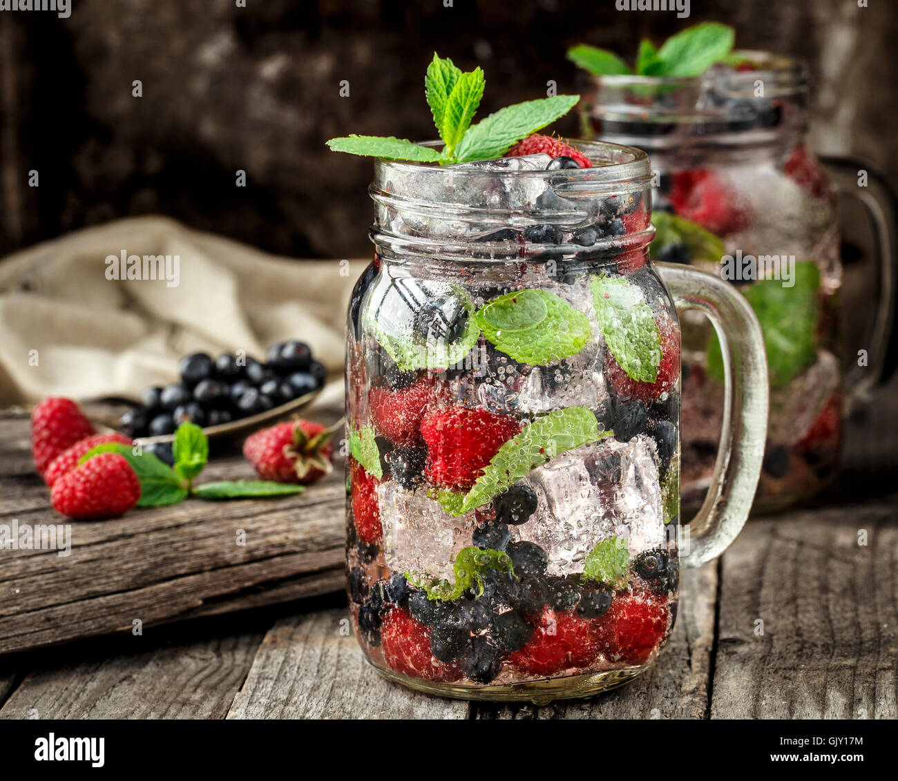 Detox Getränk mit frischen Beeren, Minze und Eis im Glas auf hölzernen Hintergrund Stockfoto