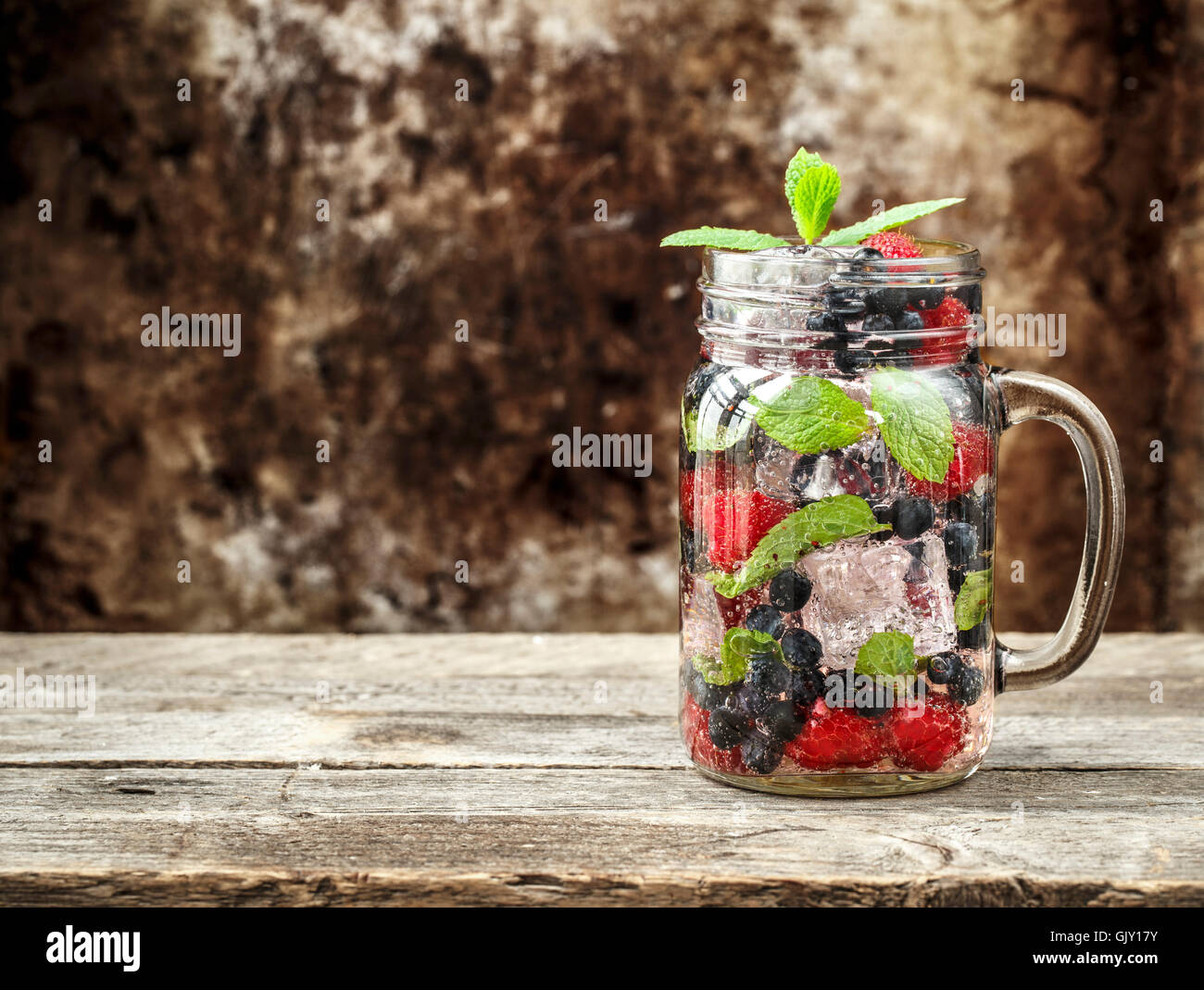 Detox Getränk mit frischen Beeren, Minze und Eis im Glas auf hölzernen Hintergrund Stockfoto