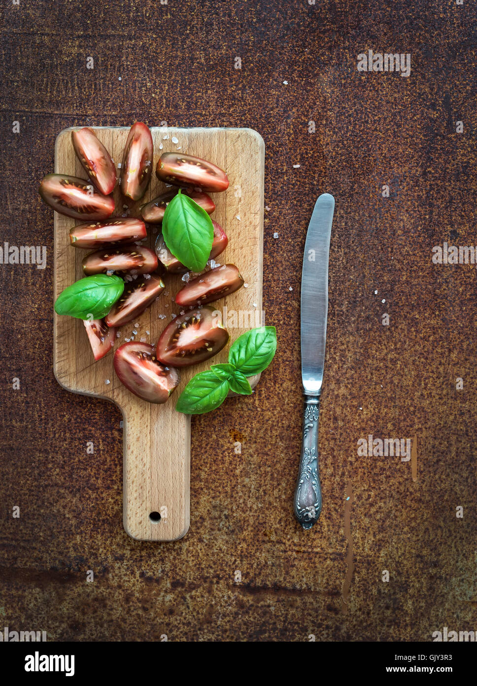 Frische Tomaten Scheiben mit Salz und Basilikum auf Schneidbrett aus Holz über Grunge Metall rostig Hintergrund, Ansicht von oben Stockfoto