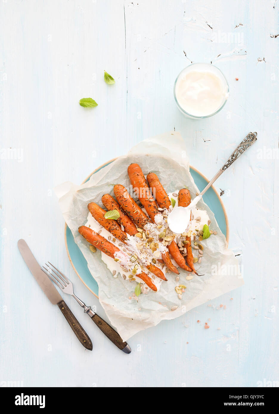 Gebratene Karotten mit Käse-Sahne-Sauce auf blaue Platte über Licht blau lackierten hölzernen Hintergrund, Draufsicht, vertikale Zusammensetzung Stockfoto