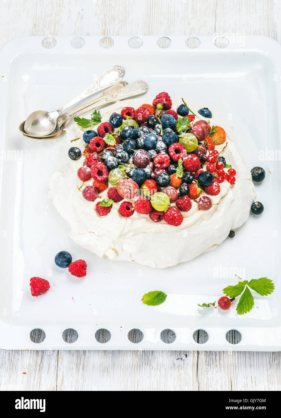 Pavlova Kuchen mit frischen Garten Beeren serviert mit silbernen Löffel auf weißen Backblech über weiß bemalte hölzerne Hinterg Stockfoto