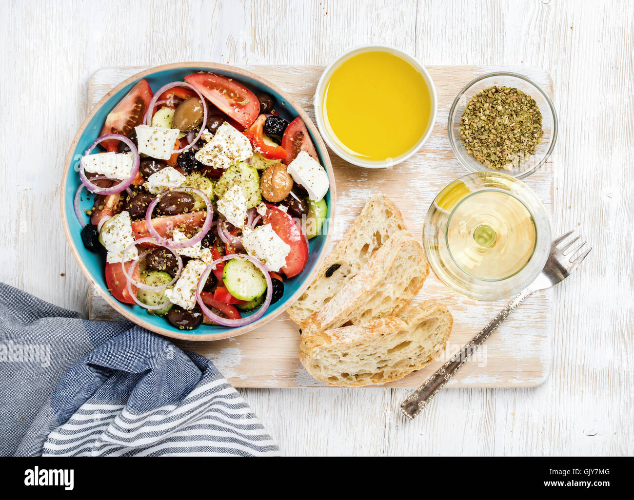 Griechischer Salat mit Glas Weißwein über alte weiß lackierten Holzplatte, Draufsicht, horizontale com, Oregano, Olivenöl und Brot Stockfoto