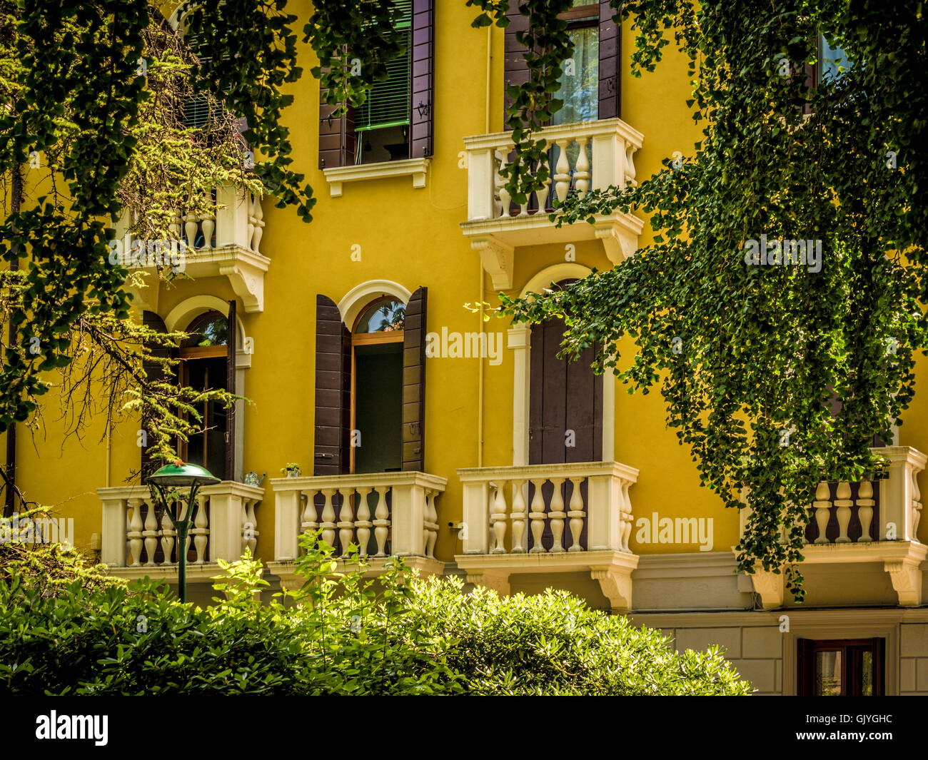 Traditionelles, in Gelb gehaltenes Gebäude mit Fensterläden und Jalousien an den Bogenfenstern. Venedig, Italien. Stockfoto