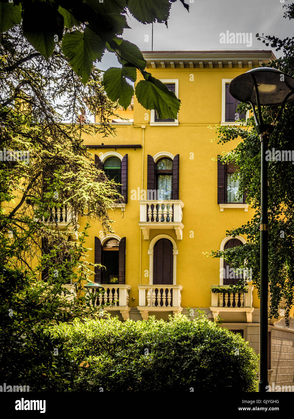 Traditionelles, in Gelb gehaltenes Gebäude mit Fensterläden und Jalousien an den Bogenfenstern. Venedig, Italien. Stockfoto