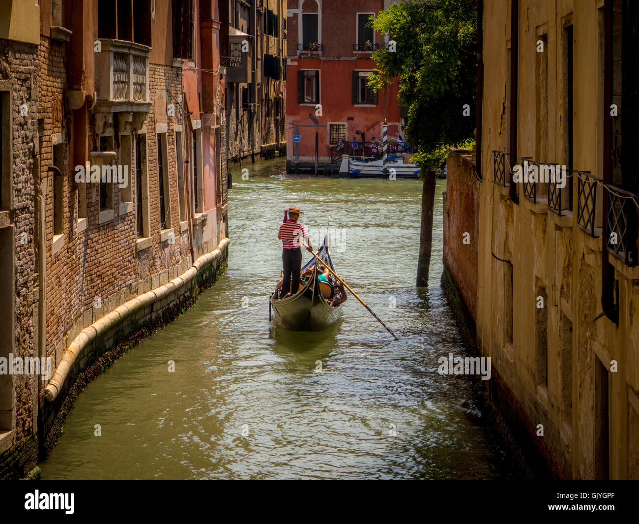 Einzelne Gondoliere mit einem traditionellen Strohhut Hut und gestreiften Oberteil treibt seine Gondel an einem Kanal entlang. Venedig, Italien. Stockfoto
