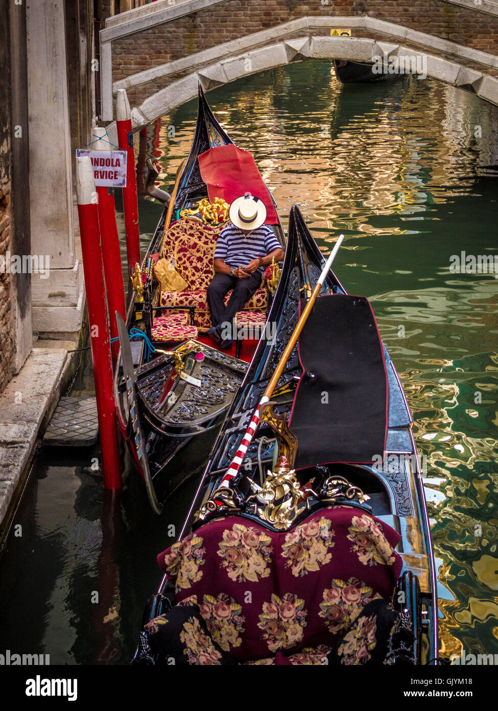 Gondoliere tragen traditionelle gestreiften Oberteil und Stroh Strohhut Hut sitzt in seinem Boot eine SMS auf sein Handy. Stockfoto