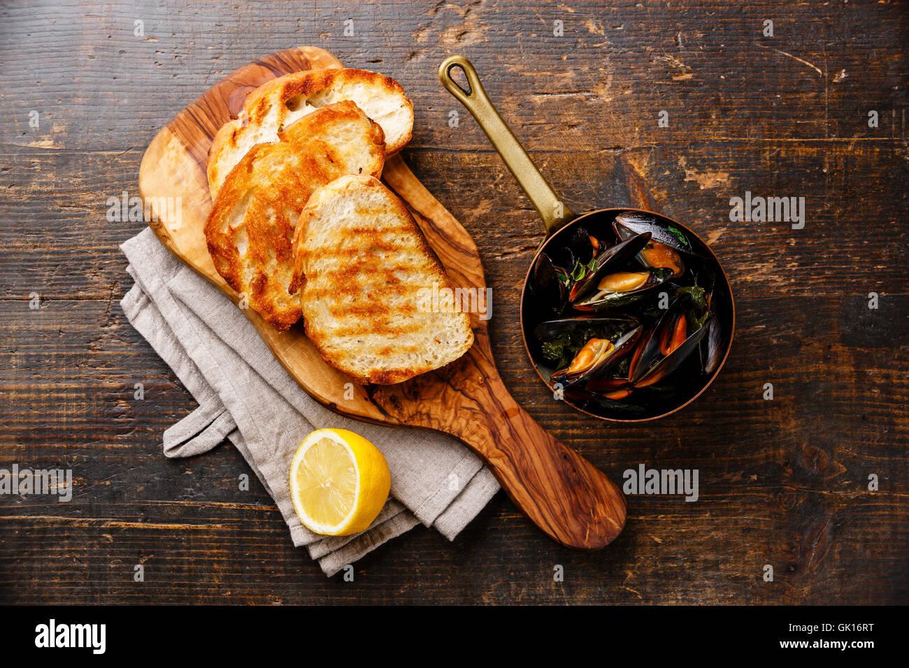 Muscheln im Kupferkessel, Brot, Toast und Zitrone auf hölzernen Hintergrund Stockfoto