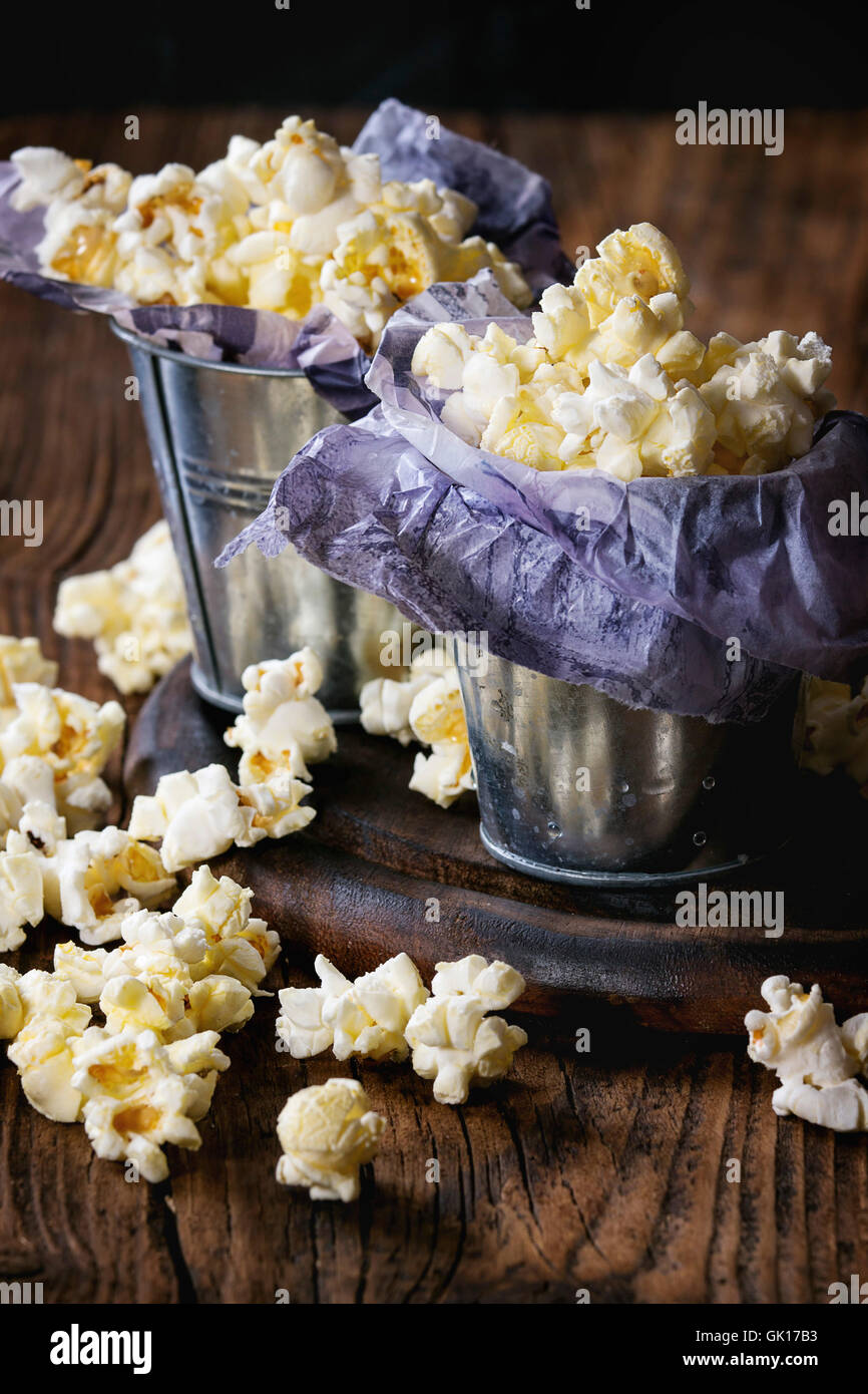Vorbereitete gesalzene Popcorn serviert in kleinen Eimern mit Papier innen auf Holz Schneidebrett in dunklem Holz. Stockfoto