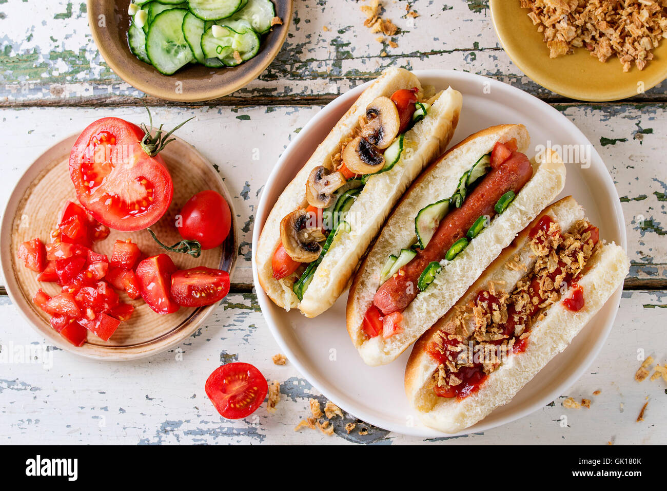 Auswahl an hausgemachten Hot Dogs mit Wurst, gebratenen Zwiebeln, Tomaten und Gurken, serviert mit Zutaten in großen weißen Teller ove Stockfoto