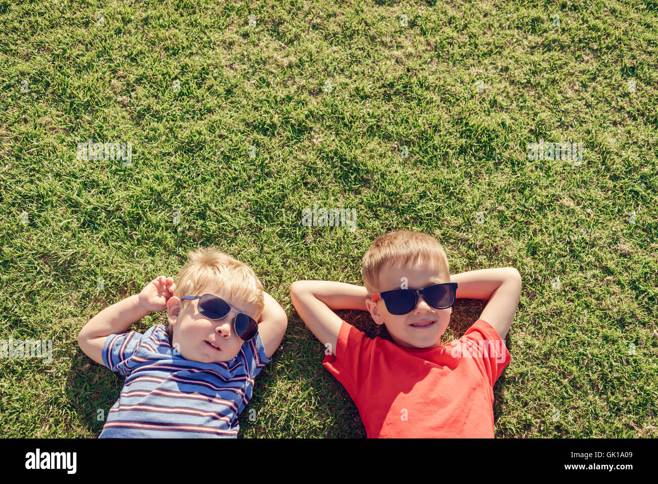 Glücklich lächelnde Kinder entspannend auf dem grünen Rasen unter Sonne, Draufsicht mit Textfreiraum. Farbe-toning angewendet Stockfoto
