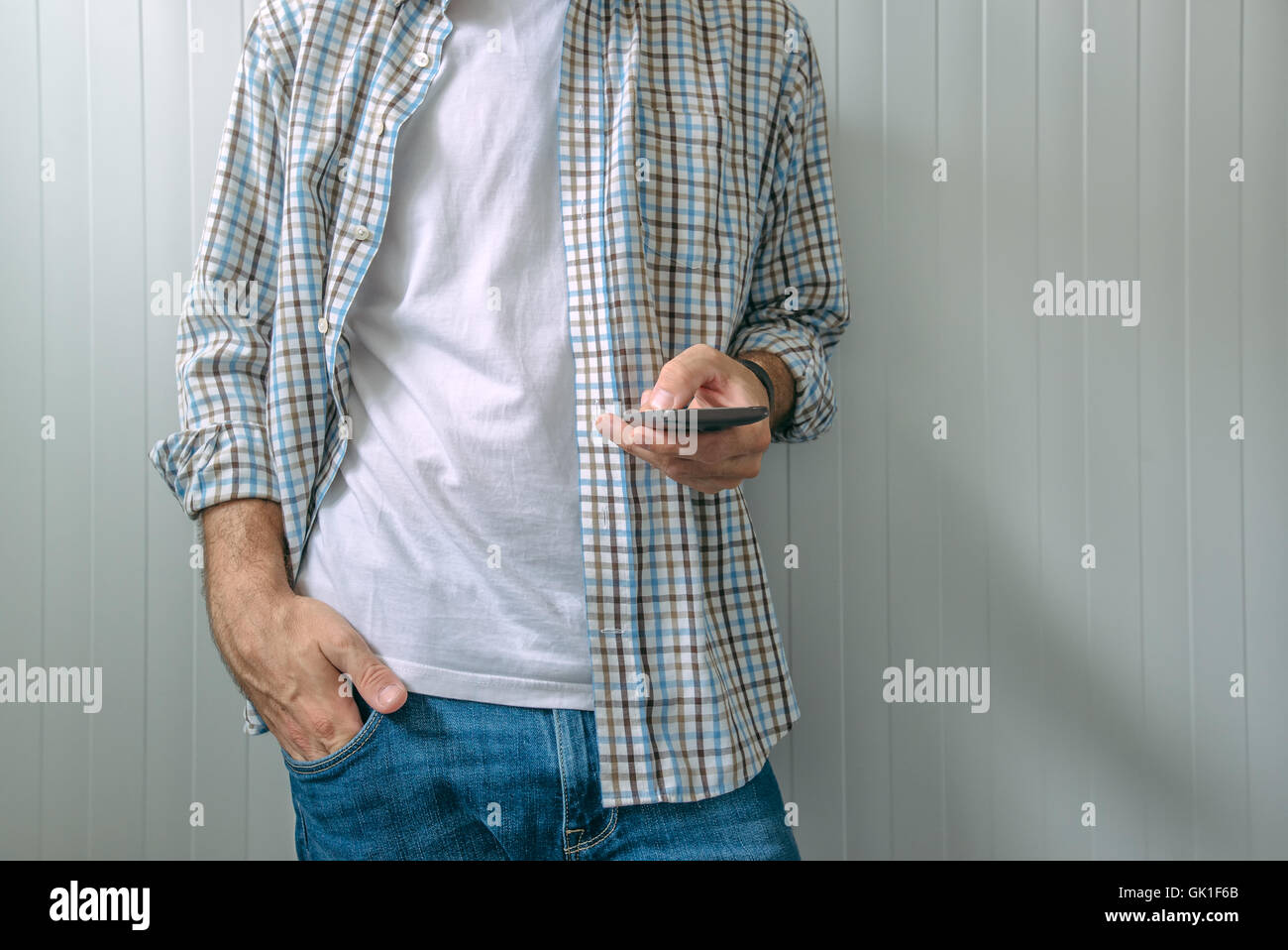 Gelangweilt legerer Mann im karierten Hemd mit Handy, Zeit zu verschwenden Stockfoto