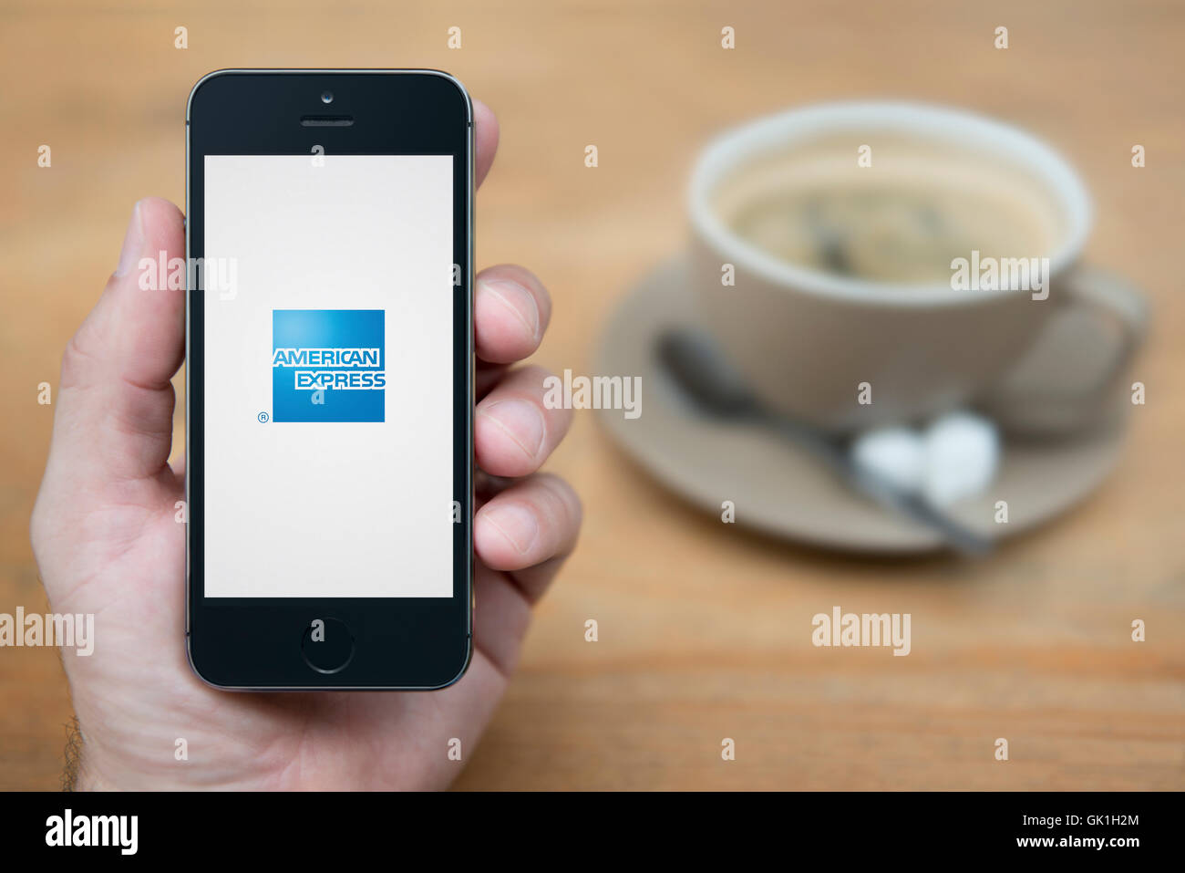 Ein Mann schaut auf seinem iPhone das das American Express Logo anzeigt, während bei einer Tasse Kaffee (nur zur redaktionellen Verwendung) saß. Stockfoto