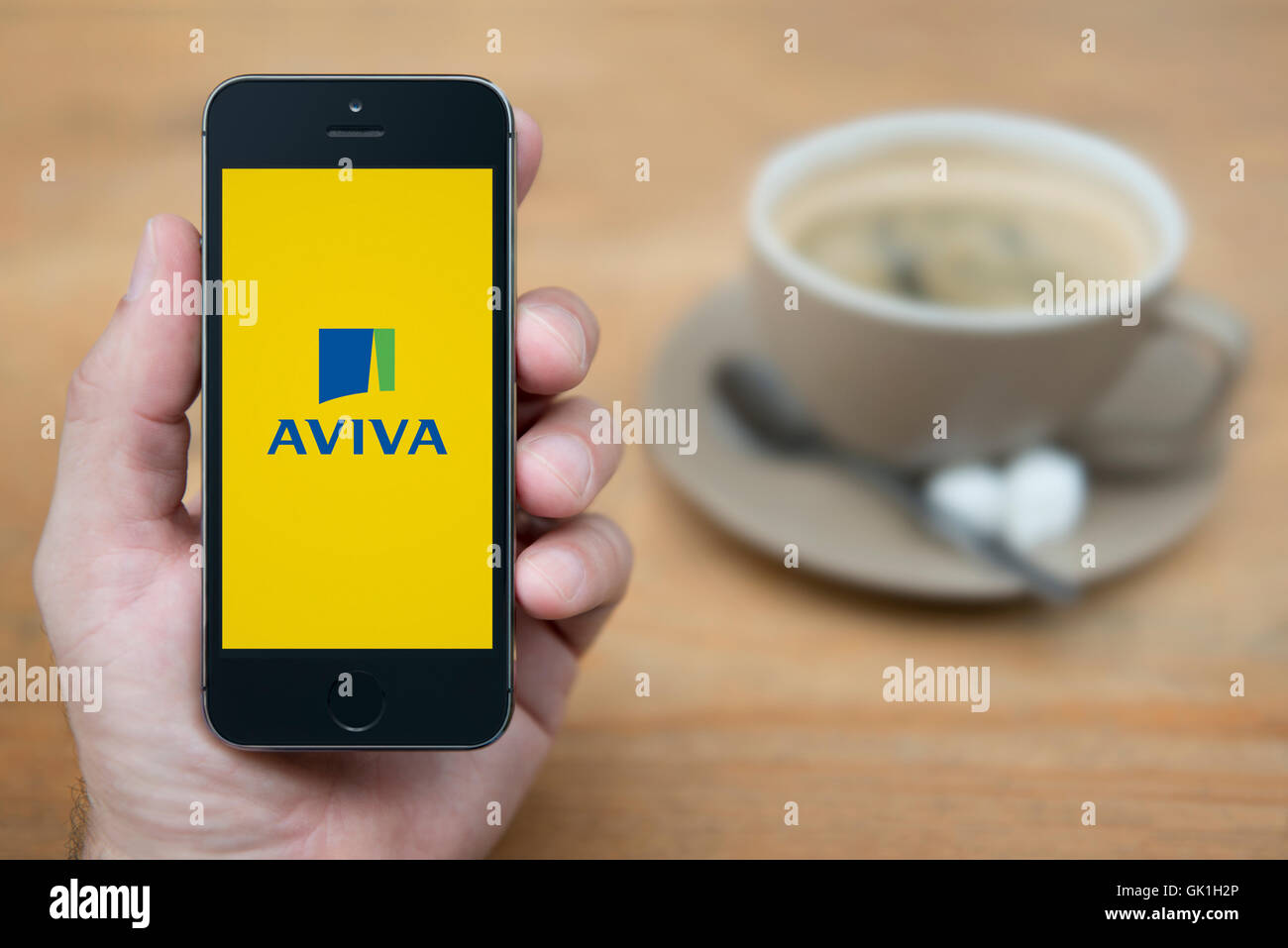Ein Mann schaut auf seinem iPhone die Aviva-Logo anzeigt, während bei einer Tasse Kaffee (nur zur redaktionellen Verwendung) saß. Stockfoto