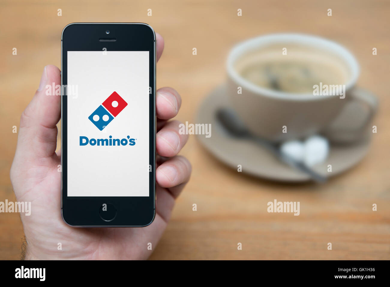 Ein Mann schaut auf seinem iPhone die die Domino-Logo anzeigt, während mit einer Tasse Kaffee (nur zur redaktionellen Verwendung) saß. Stockfoto