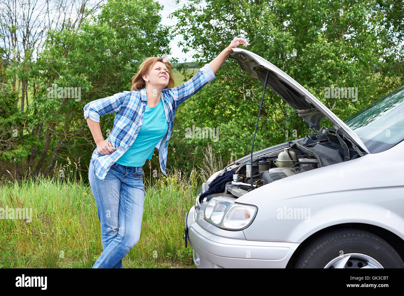 Frau mit Schraubenschlüssel in der Nähe von ihr kaputtes Auto Stockfoto