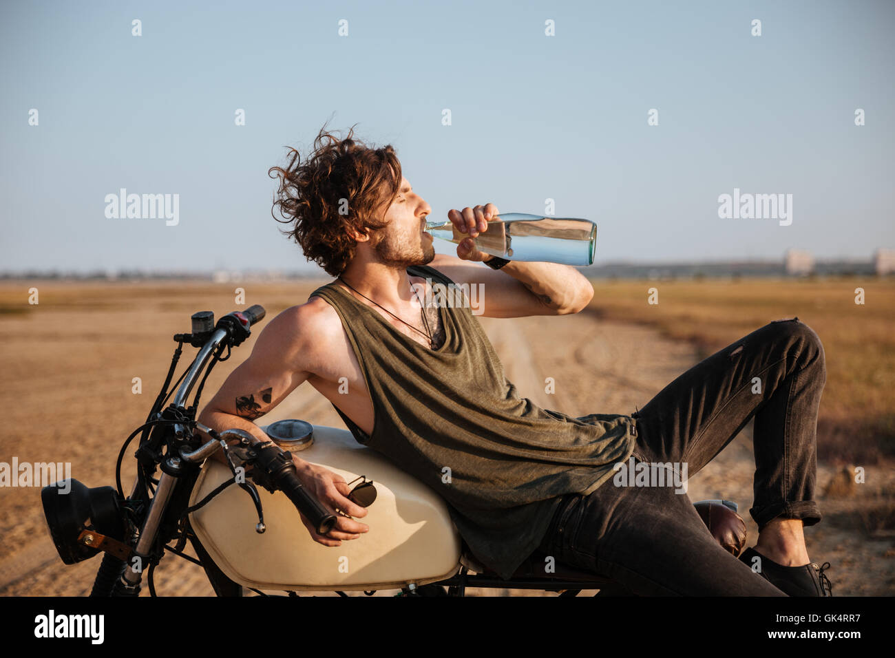 Brutale Jüngling Verlegung auf seinem Motorrad in der Wüste und Trinkwasser Stockfoto