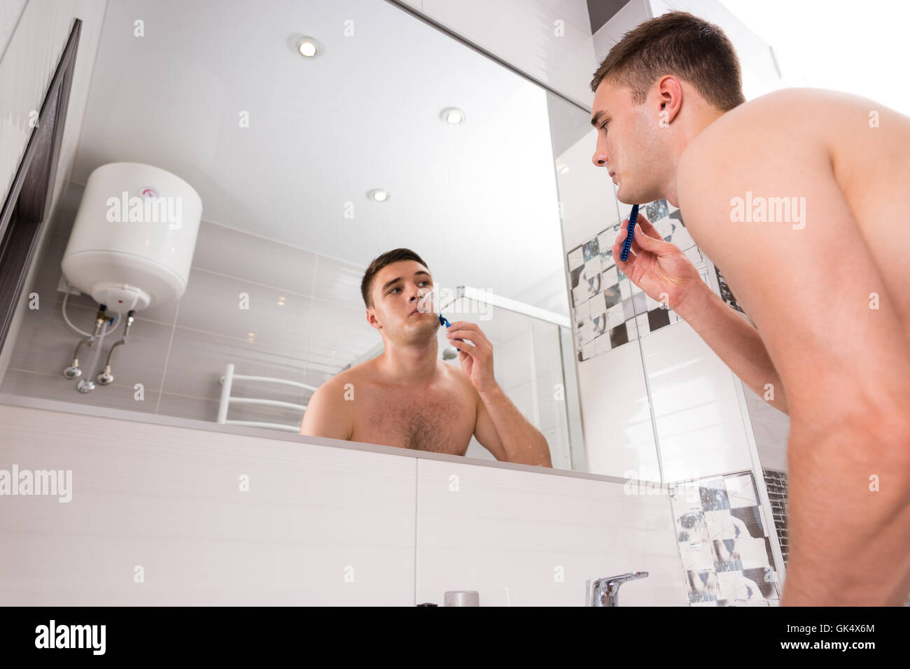 Unteransicht des männlichen rasieren sein Gesicht stand vor Spiegel in das modern geflieste Bad zu Hause Stockfoto