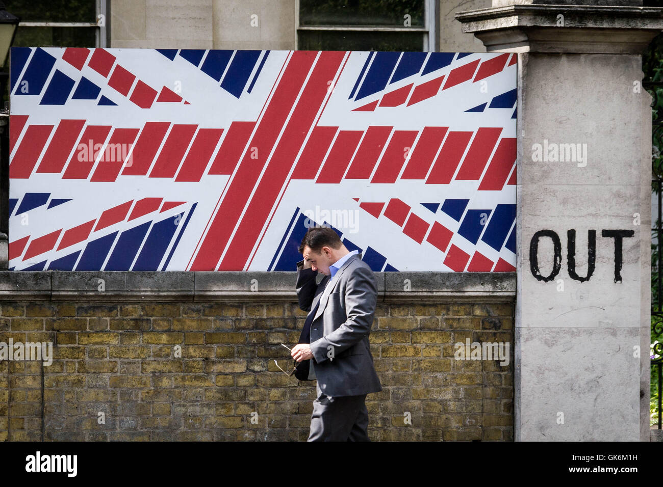 UK Brexit dokumentarische Bild. Ein London Stadt Arbeiter geht eine britische Nationalflagge Wandgestaltung. "OUT" steht auf den Ausgang zu einer lokalen Residenz, London, Stockfoto