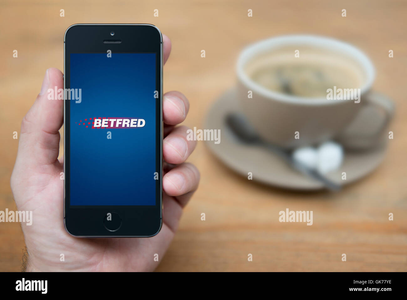 Ein Mann schaut auf seinem iPhone die Betfred-Logo anzeigt, während bei einer Tasse Kaffee (nur zur redaktionellen Verwendung) saß. Stockfoto
