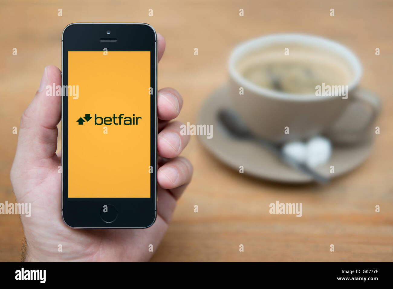 Ein Mann schaut auf seinem iPhone die Betfair-Logo anzeigt, während bei einer Tasse Kaffee (nur zur redaktionellen Verwendung) saß. Stockfoto