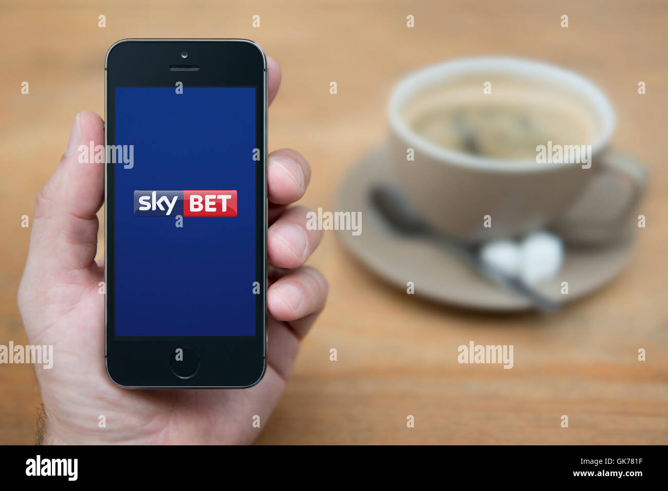 Ein Mann schaut auf seinem iPhone die Sky Bet-Logo anzeigt, während bei einer Tasse Kaffee (nur zur redaktionellen Verwendung) saß. Stockfoto