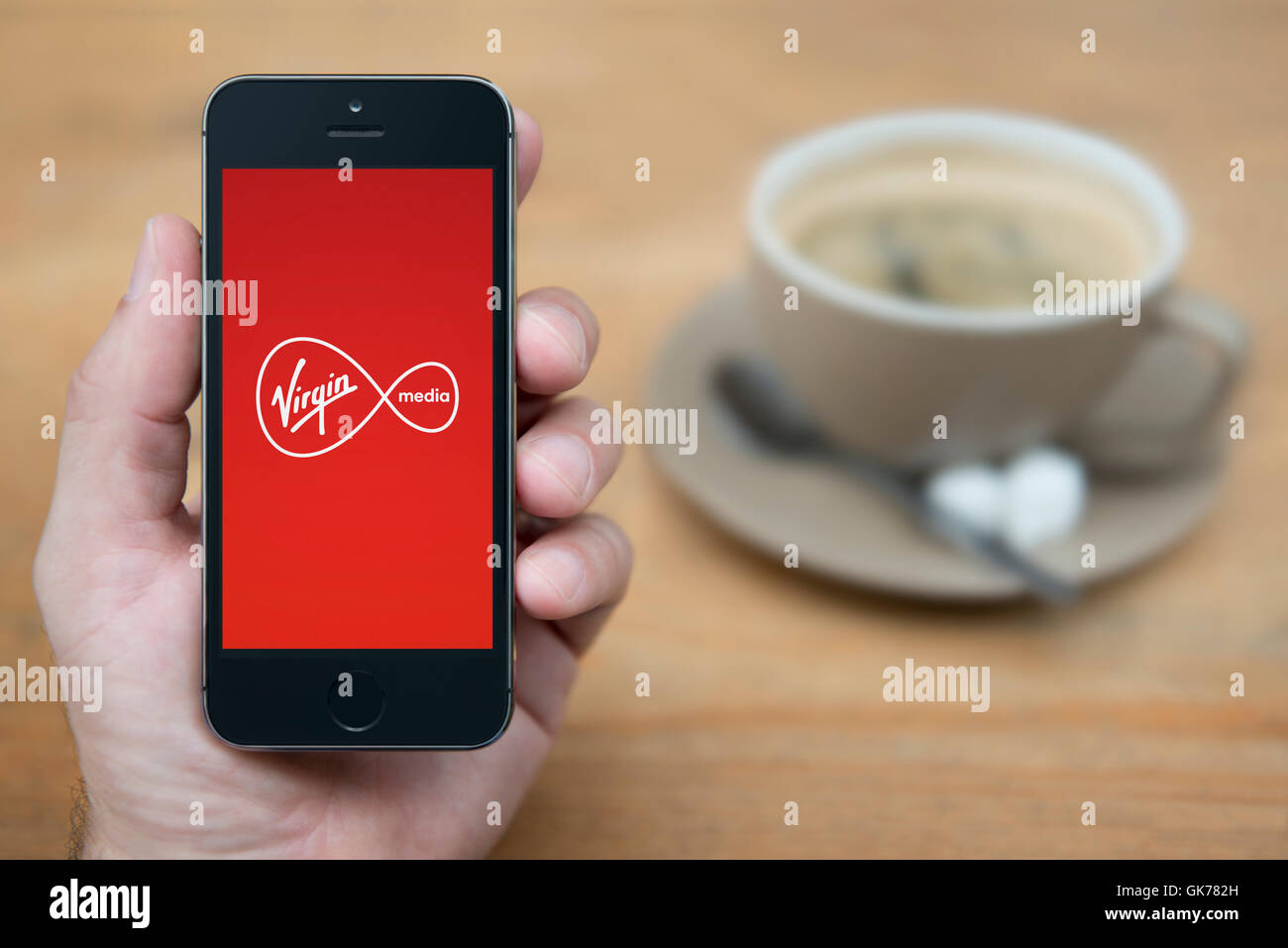 Ein Mann schaut auf seinem iPhone die Virgin Media-Logo anzeigt, während bei einer Tasse Kaffee (nur zur redaktionellen Verwendung) saß. Stockfoto
