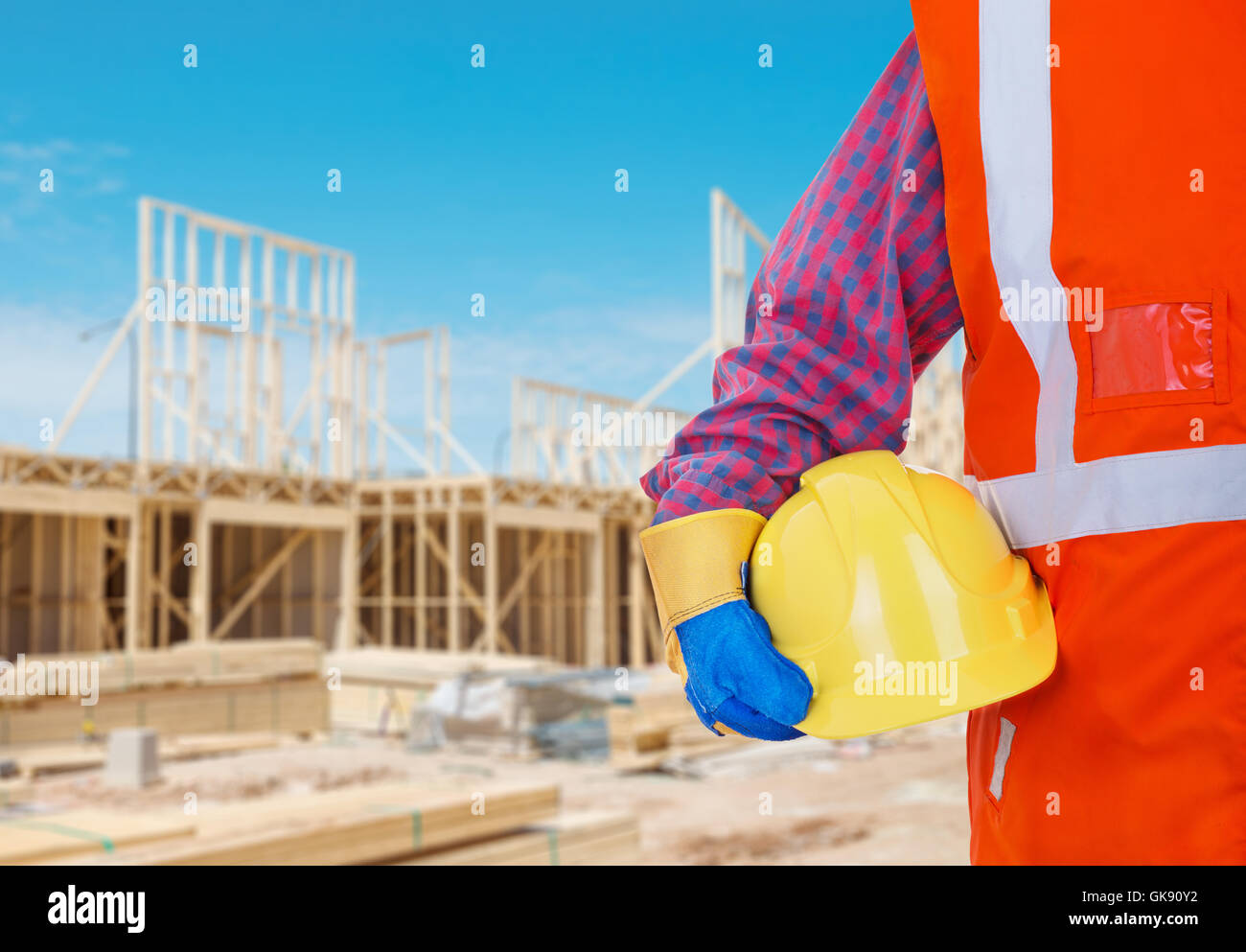 Sicherheit Schutz Arbeitsmittel. Arbeiter in orange Weste mit gelben Helm gegen Baustelle als Hintergrund Stockfoto