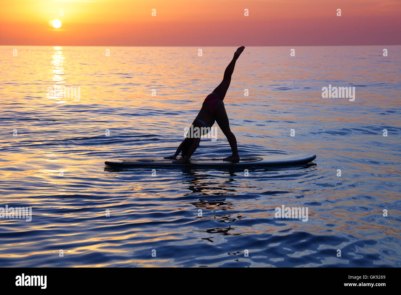 Sportliche Frauen Yoga-Übung am Strand über schöne Sonnenuntergang Hintergrund, stehend auf dem Sup-Board auf dem Wasser Stockfoto