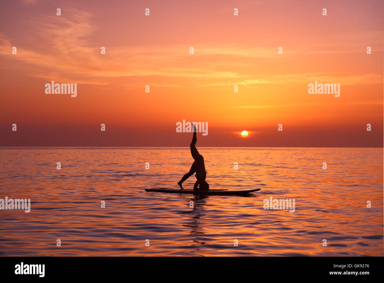 Silhouette von einem Yogalehrer balancieren auf Paddel Board über schöne orange Sonnenuntergang Hintergrund, auf dem Kopf stehend Stockfoto